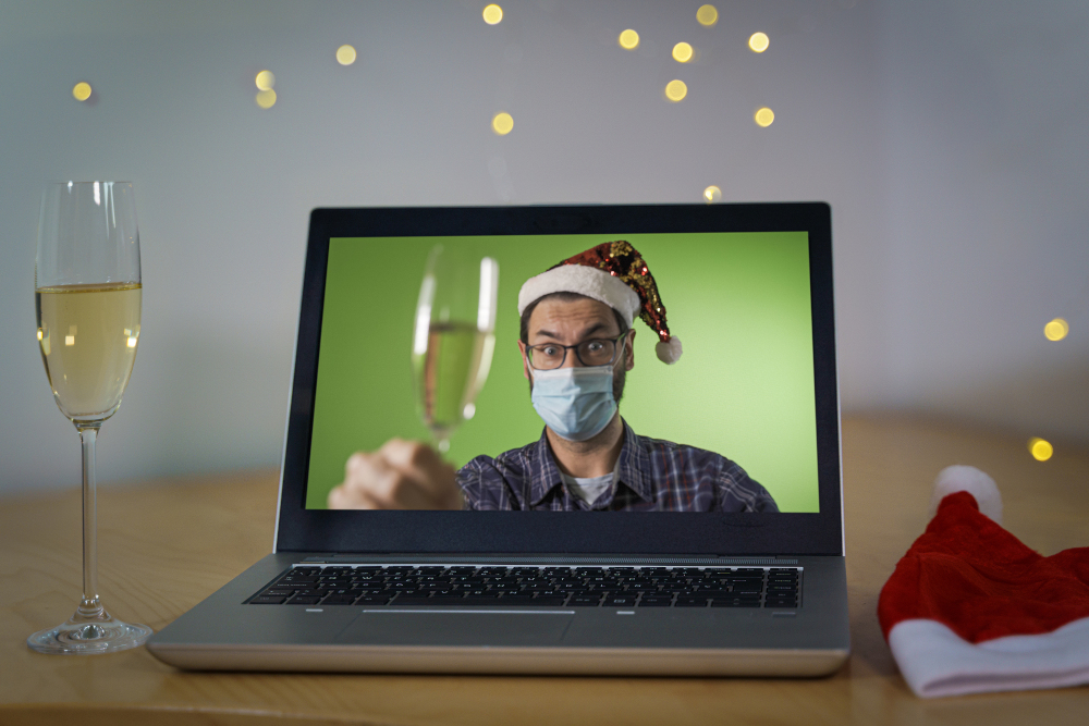Virtual Holiday Party Setup: Webcam video on laptop of man wearing santa hat and toasting with champagne