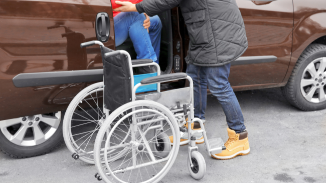 Wheelchair Accessible Van Rentals in Tallahassee and Gainesville Blog Image of an adult helping another adult out of an accessible van to a wheelchair.
