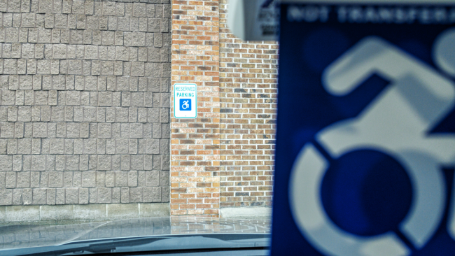 Looking through a vehicle's windshield with the handicap car tag in the background to see a handicap parking decal affixed to a brick column