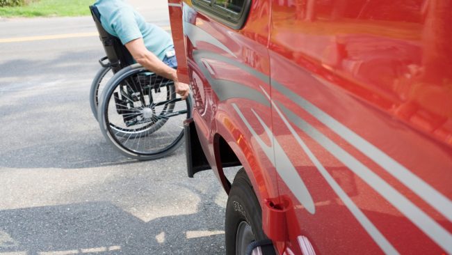 NMEDA QAP Certified Blog Image; back end of a car with a person in a wheelchair in the background.