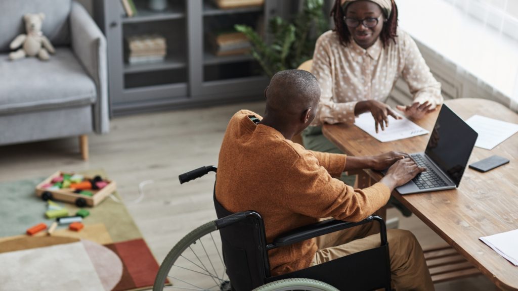 man in wheelchair on laptop with a woman sitting next to him